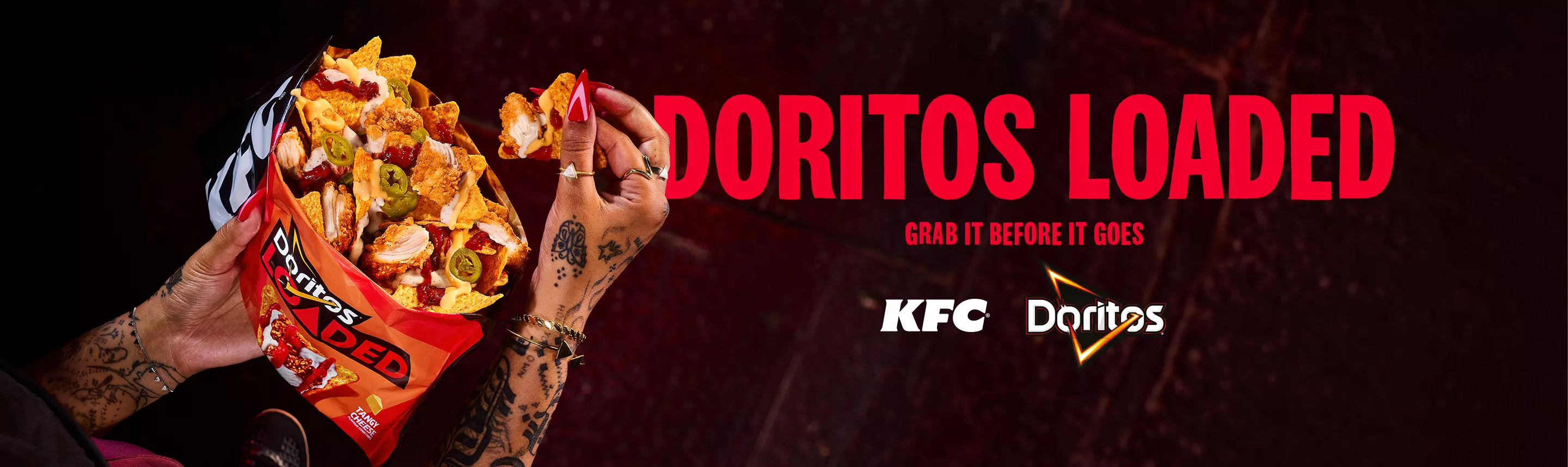 Two tattooed hands hold open a Doritos Loaded bag filled with nacho chips, KFC Crispy Tenders, guacamole and jalapeños, with "Doritos Loaded, grab it before it goes" and the KFC and Doritos logos on a dark red background.